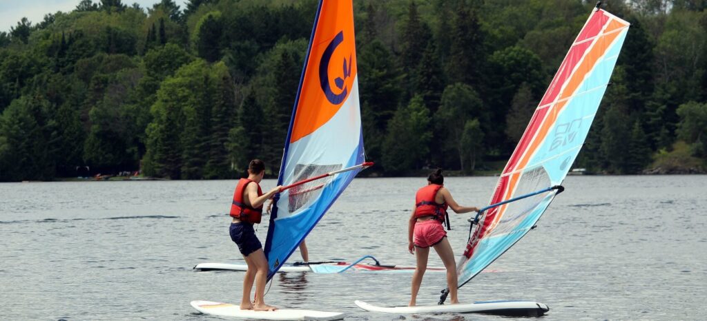 Summer campers sailboarding on a lake.